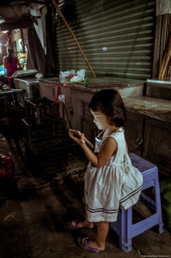 Em bé ngồi chơi một mình khi mẹ dọn hàng lúc tám giờ tối, chợ Căn Cứ, Gò Vấp, 2018